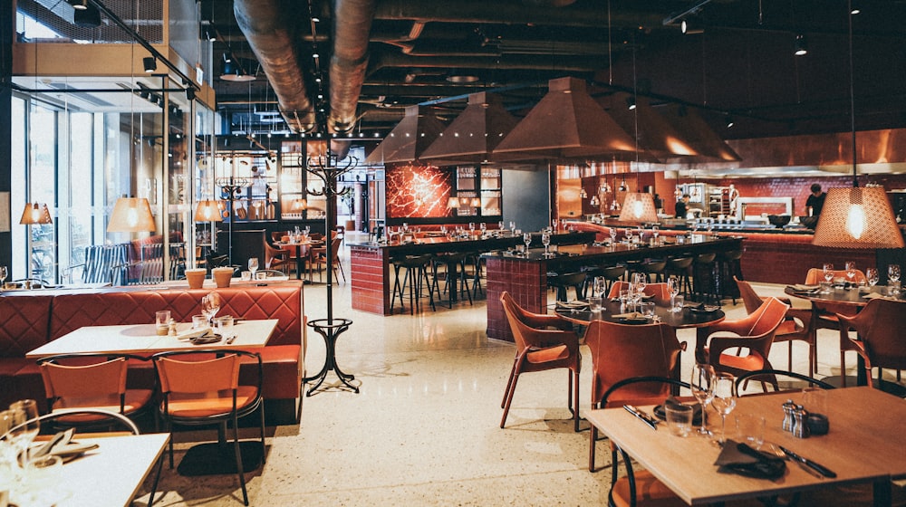 A restaurant diner scanning a QR code on a wooden table with a smartphone, the digital menu showing dish photos and prices on screen, while a waiter carries plates through the softly lit dining room in the background.